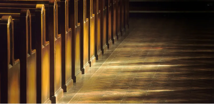 Rows of wooden church pews beside a sunlit sanctuary floor